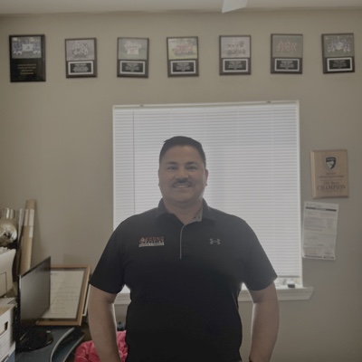 Mario Espindola, Founder of Econo Roofing, in his Delhi CA office with framed manufacturer certifications on the wall behind him: Owens Corning Platinum Preferred, GAF Master Elite, CertainTeed Select ShingleMaster, and others.