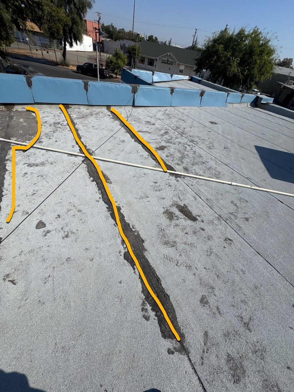 Gray bitumen commercial roof with yellow spray markings tracing existing seam cracks — diagnostic estimate documentation by Econo Roofing at Beto's Bakery Modesto.