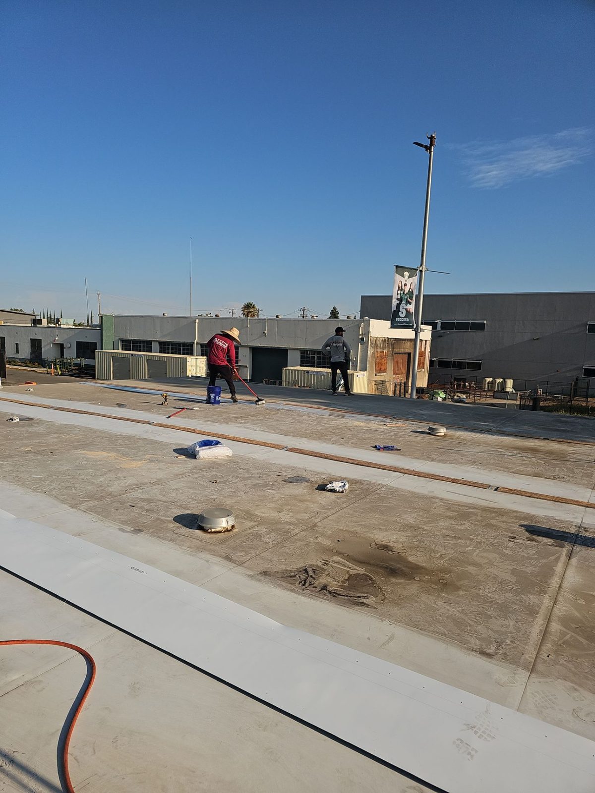 Econo Roofing crew in red shirts applying TPO coating on Manteca High School roof