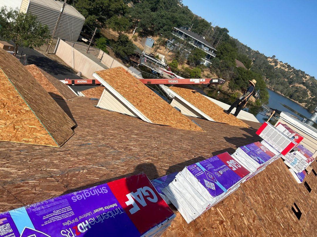 Crew working on exposed roof deck with GAF shingle bundles, complex multi-hip roof geometry