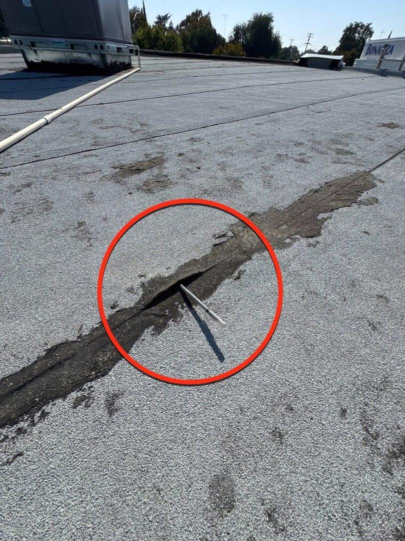 Close-up of nail pop and seam crack circled in red on flat roof
